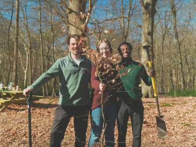 Drei Personen stehen mit Schaufeln im Wald