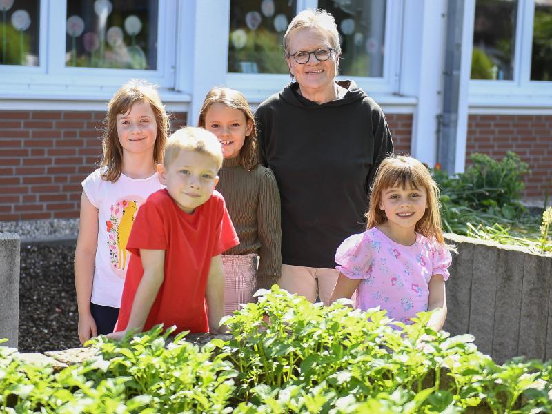 Betreuerin steht mit vier Kindern an einem bepflanzten Hochbeet