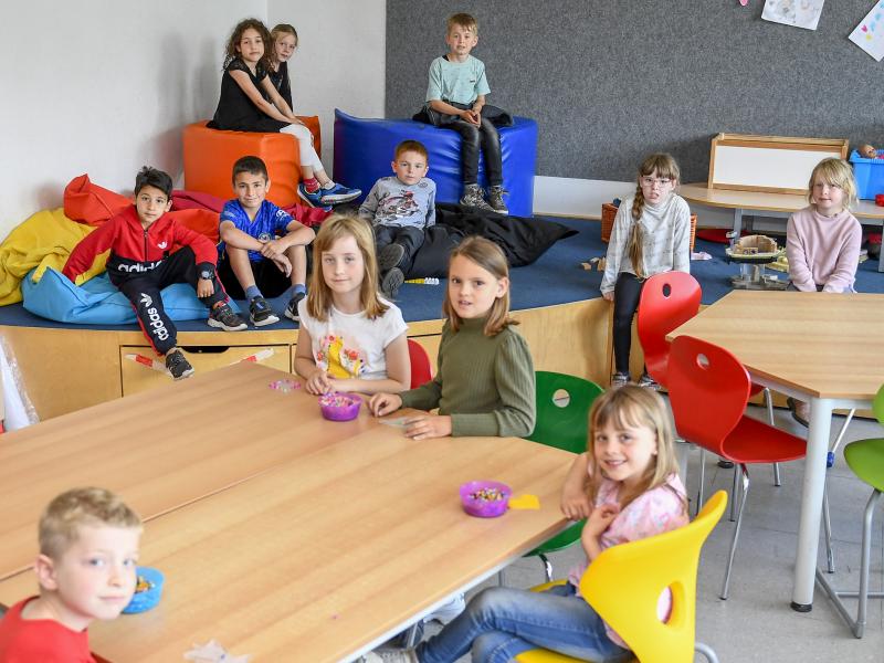 Kinder sitzen im Vordergrund an Tischen, im Hintergrund auf einer kleinen Empore mit begehbaren Spielklötzen
